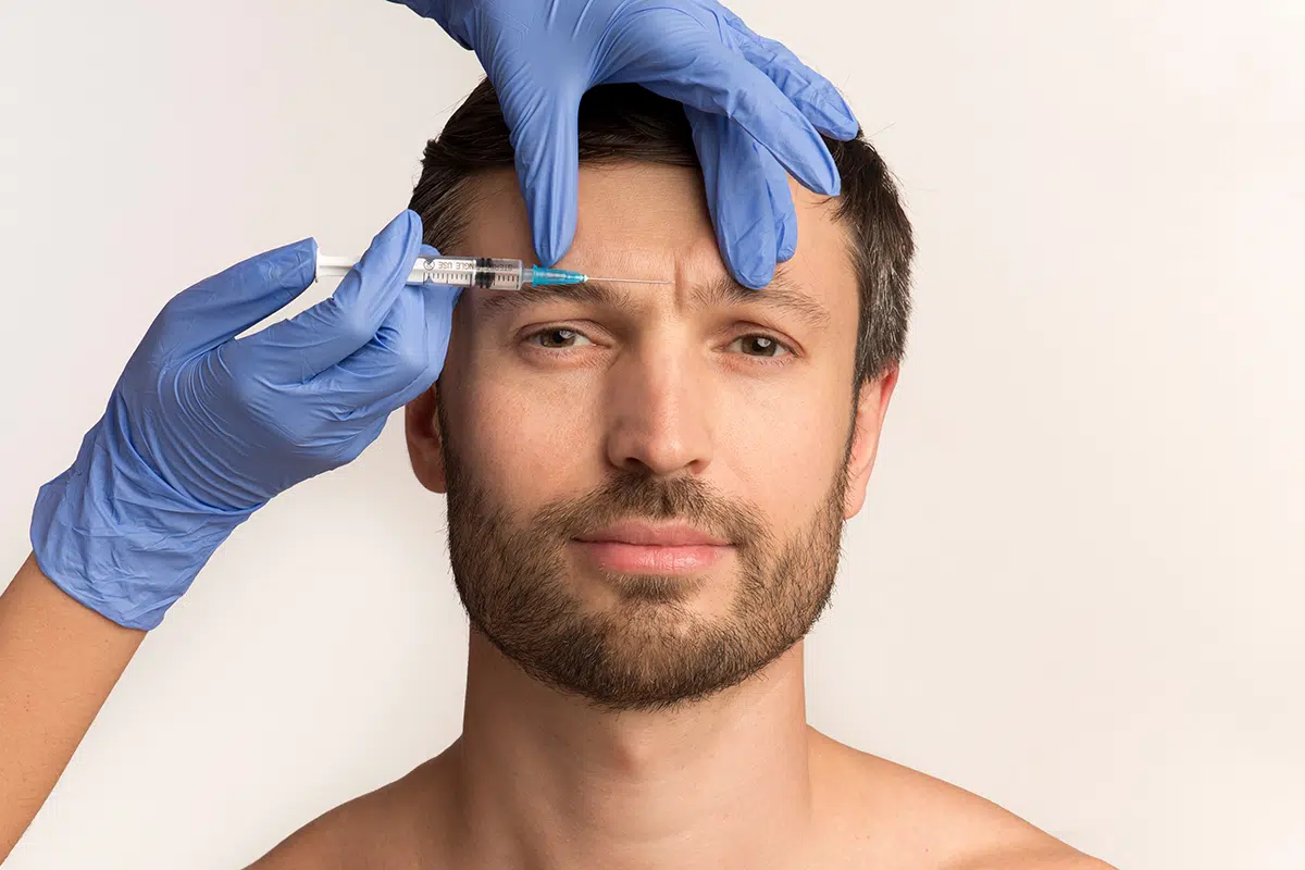 a man receives an injection to his forehead from a doctor wearing blue gloves