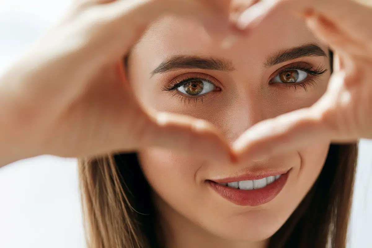 beautiful happy woman showing love sign near eyes