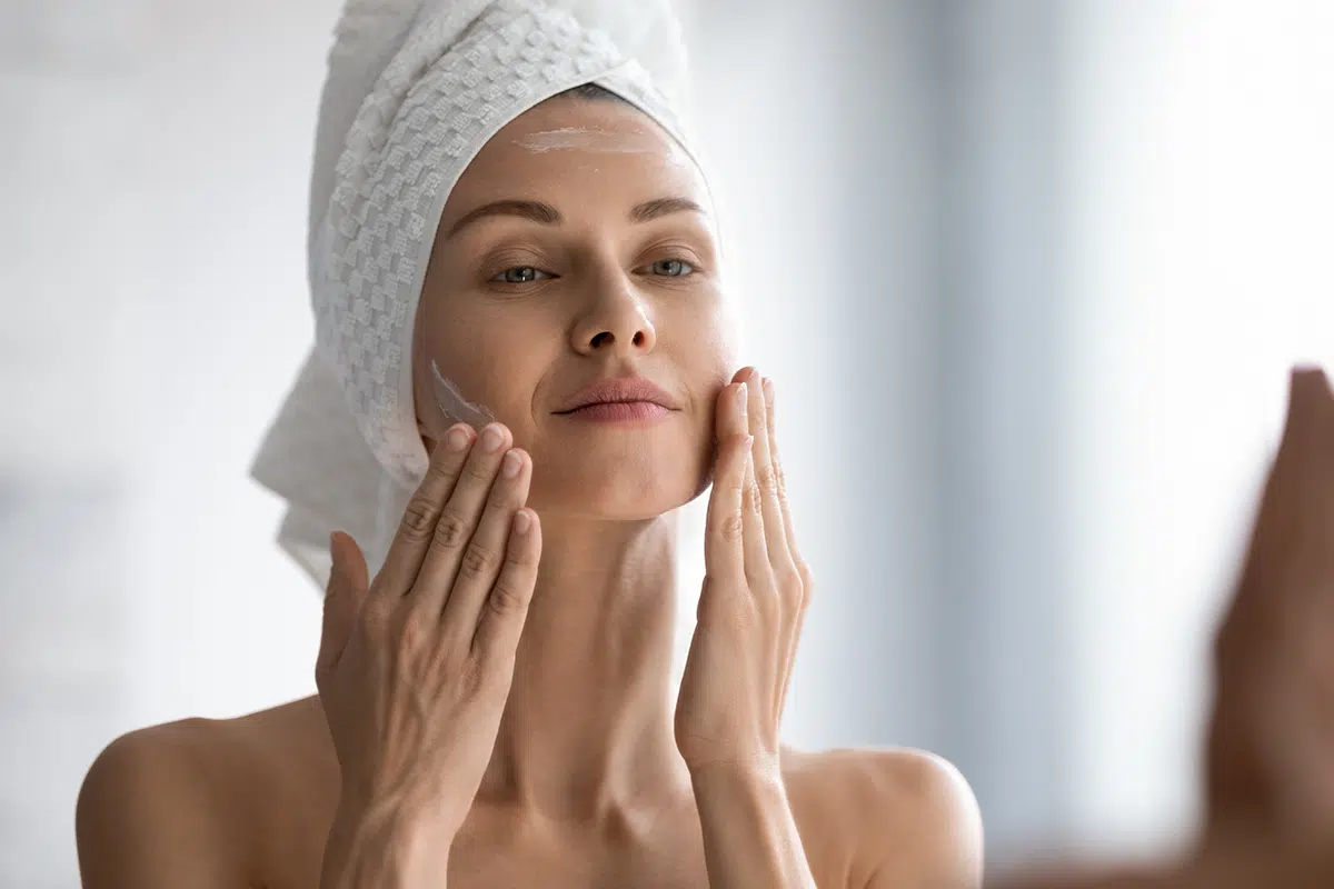 beautiful woman applying moisturizing creme on face after shower