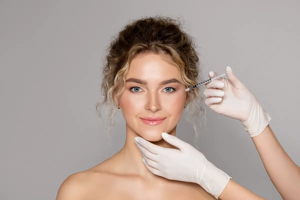 cosmetologist doctor making botox injection for eyes area to young lady