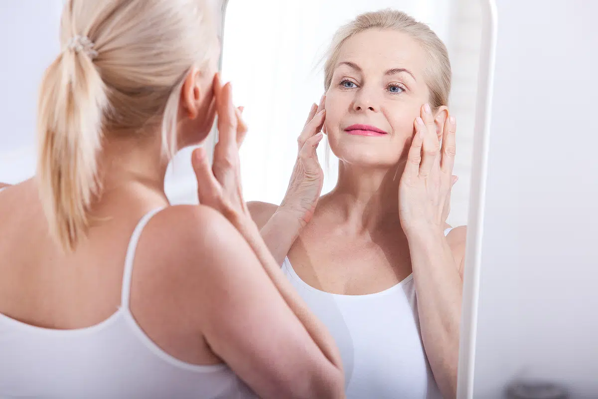 middle aged woman looking at wrinkles in mirror